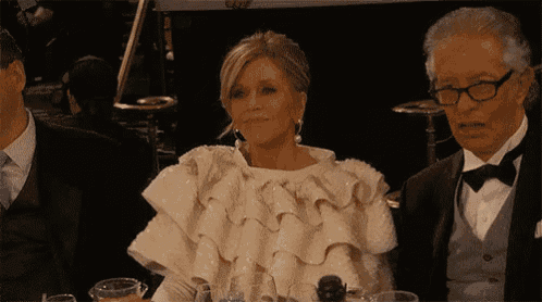 a woman in a white ruffled top is sitting at a table with two men in tuxedos .