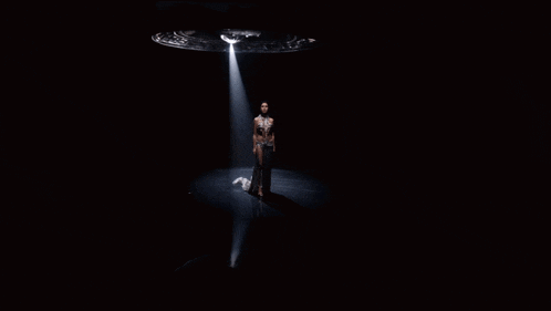 a woman is standing in a spotlight with a light coming out of a saucer