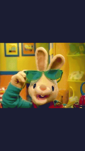 a stuffed bunny wearing sunglasses is standing in front of a yellow wall