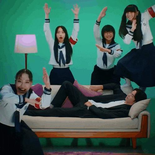 a group of people are standing around a man laying on a couch with his arms in the air