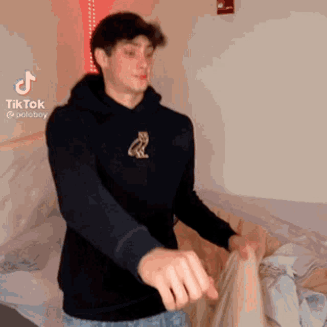 a young man wearing a black hoodie is standing in front of a bed .