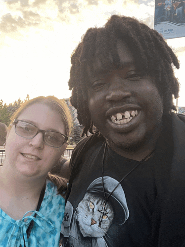 a man and a woman are posing for a picture and the man is wearing a cat shirt with a cross on his neck