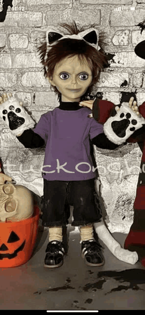 a doll wearing a cat ear headband and paw gloves stands in front of a brick wall .