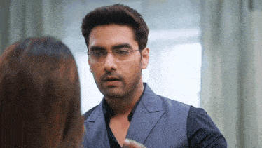 a man wearing glasses and a suit looks at a woman