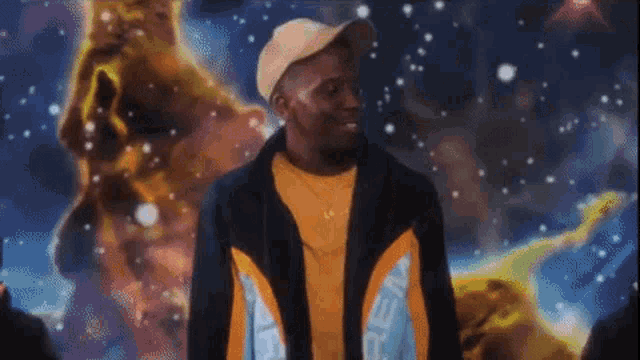 a man wearing a hat and a jacket is standing in front of a painting of space .