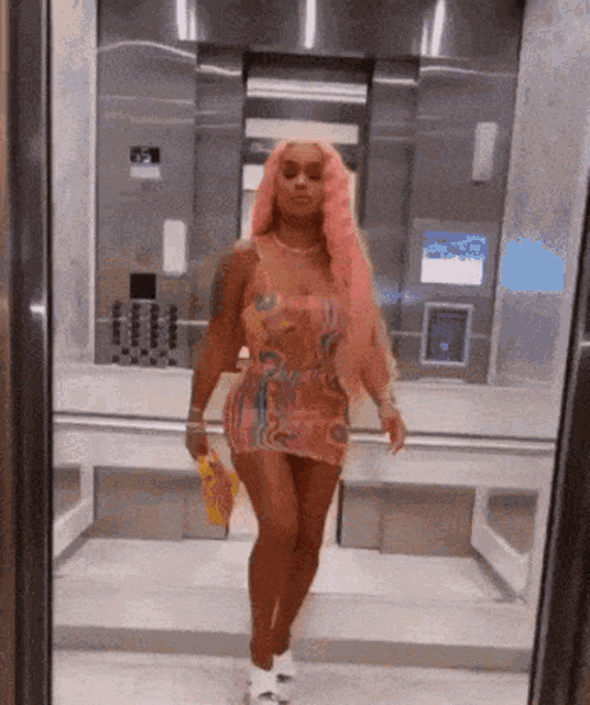 a woman in a pink dress is walking out of an elevator