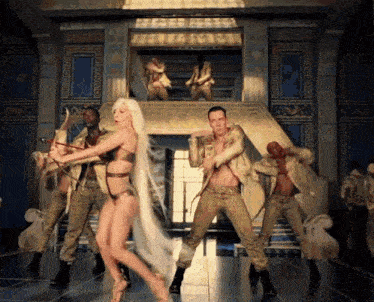 a group of people are dancing in a room with a greek key pattern on the wall