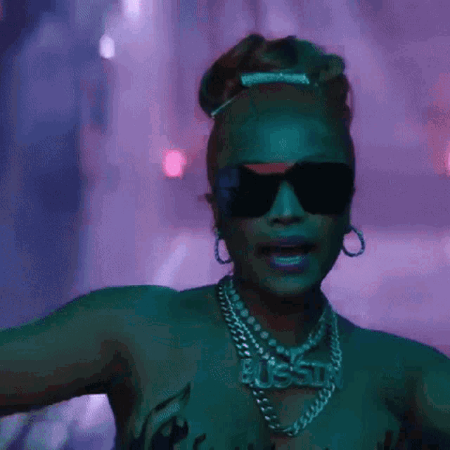 a woman wearing sunglasses , a necklace and earrings is dancing in a dark room .