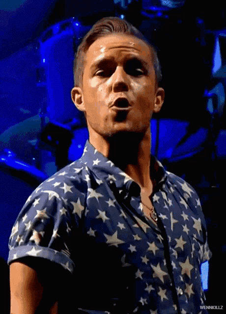 a man wearing a blue shirt with white stars on it is singing into a microphone