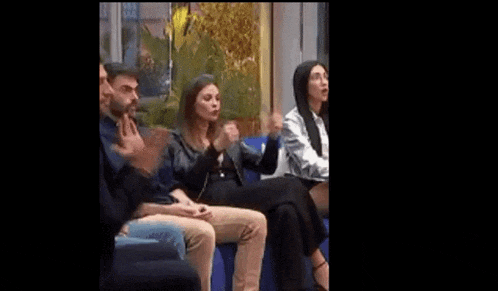 a group of people are sitting on a blue couch and clapping .