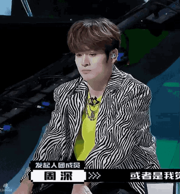 a young man wearing a zebra print jacket and a yellow shirt is sitting on a stage .