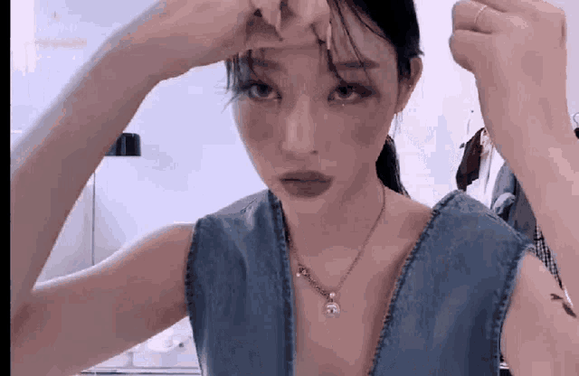 a woman wearing a blue tank top and a necklace wipes her forehead with her hands .