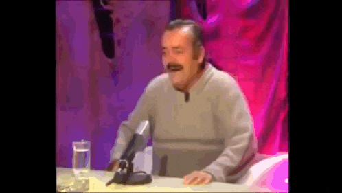 a man sitting at a table with a microphone and a glass of water .