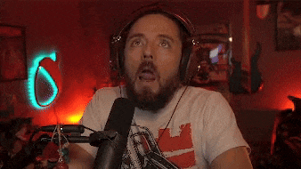 a man with a beard wearing headphones is sitting in front of a microphone and making a funny face .