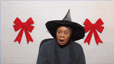 a woman wearing a witch hat stands in front of red bows on a wall