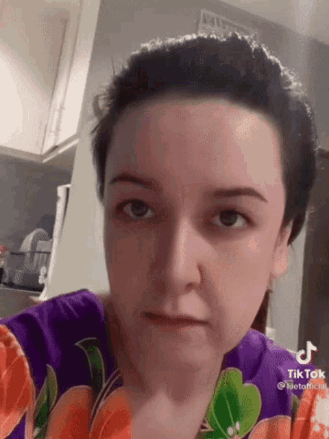 a woman wearing a purple shirt with flowers on it is making a funny face in a kitchen .