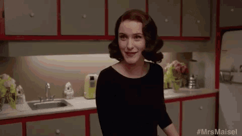 a woman in a black dress is standing in a kitchen with red cabinets .