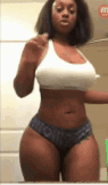 a woman is standing in front of a mirror wearing a white tank top and blue underwear .