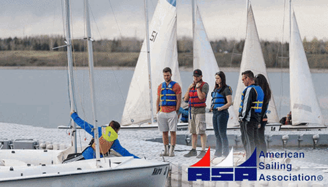 a group of people are standing on a dock next to a sailboat that has the number 51 on it