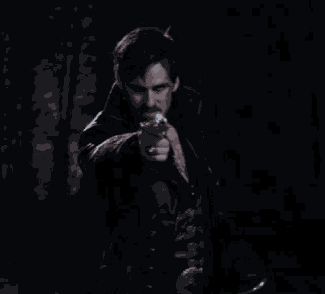a man in a leather jacket is pointing a gun in the dark