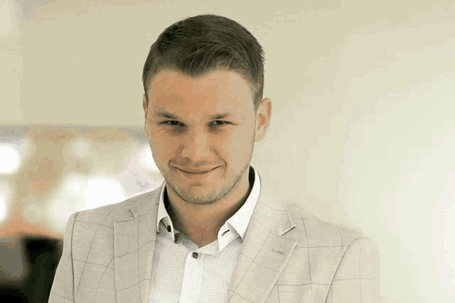 a man wearing a white shirt and a plaid jacket smiles for the camera