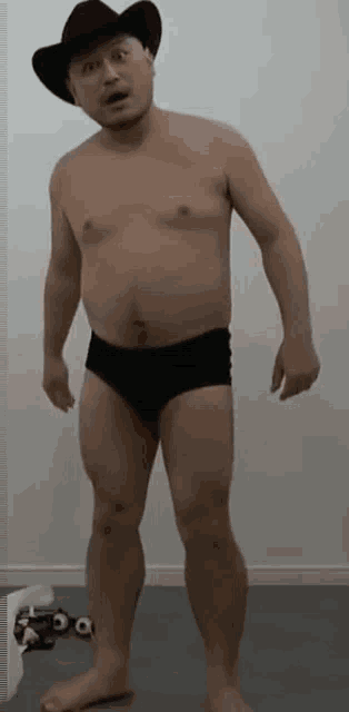 a shirtless man in black underwear and a cowboy hat is standing in a room .
