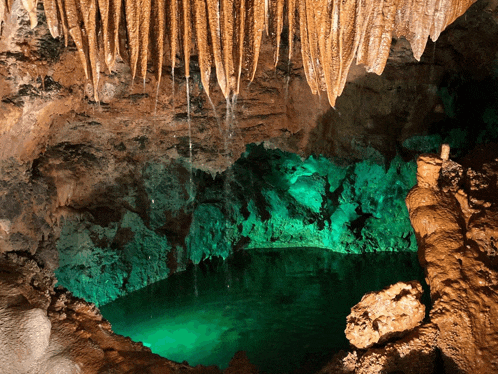 a cave with a pool of green water and icicles