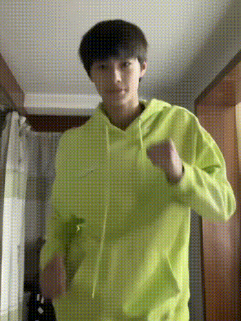 a young man is wearing a neon green hoodie and dancing in a hallway .