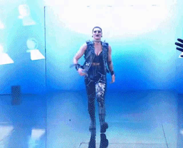 a man in a black vest and black pants is walking in front of a blue wall