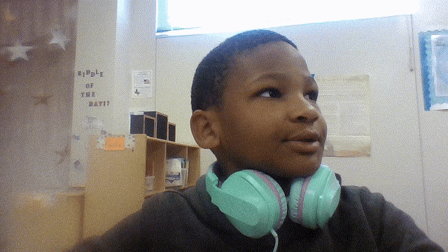 a young boy wearing headphones stands in front of a wall that says reply of the day