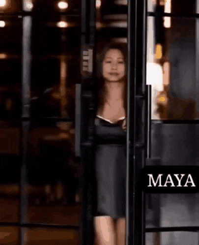 a woman in a black dress is standing in a doorway with a sign that says maya on it .