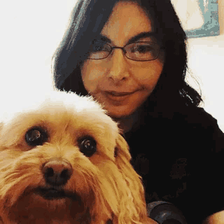 a woman with glasses holds a small brown dog