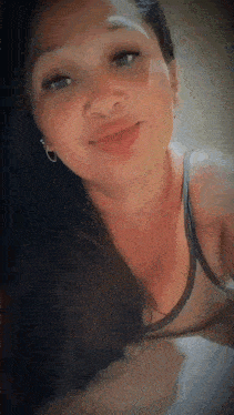 a woman wearing a tank top and earrings is smiling for the camera