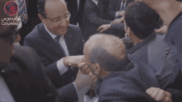 a man in a suit shakes another man 's hand in front of columbus