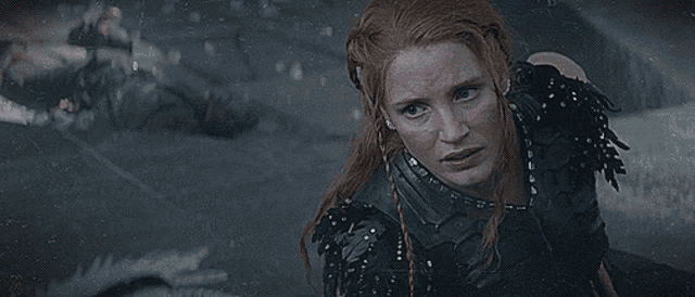 a woman with red hair is wearing a black armor and looking at something .