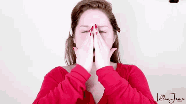 a woman in a red shirt is covering her face with her hands