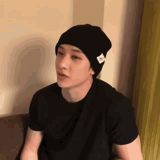 a young man wearing a black beanie and a black shirt is sitting on a couch