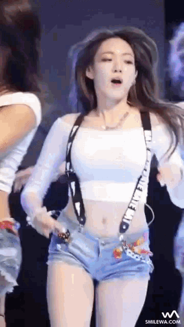a woman in a white crop top and blue shorts is dancing on stage .