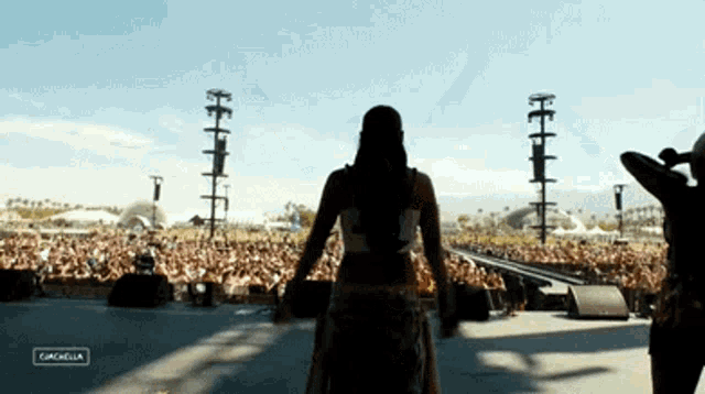 a woman stands in front of a crowd at a music festival with the word coachella in the corner