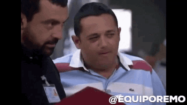 a man in a blue and red striped shirt is talking to another man in a black shirt