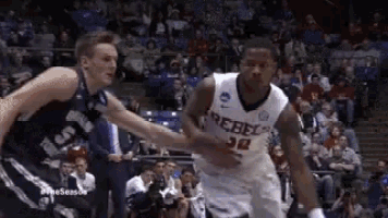 two basketball players are playing a game of basketball on a court in front of a crowd .