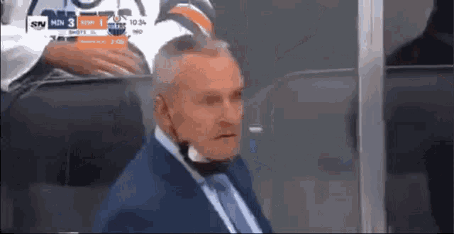a man in a suit and tie is wearing a mask while sitting in a stadium .