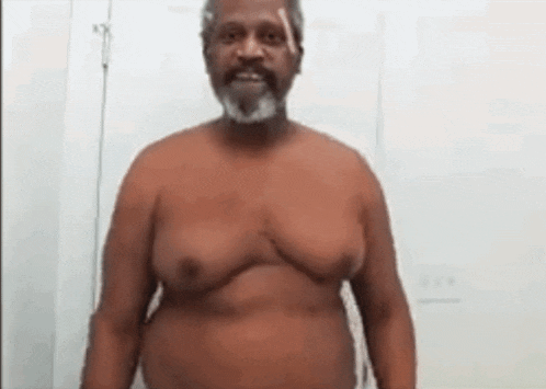 a shirtless man with a beard is standing in front of a white wall and smiling .