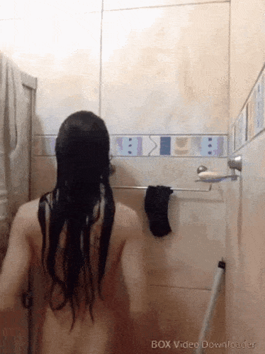 a naked woman is taking a shower in a bathroom with a towel hanging on the wall .