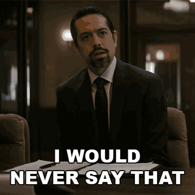 a man in a suit and tie is sitting at a desk and says i would never say that