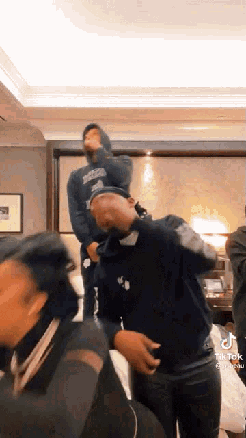 a group of people are dancing in a room with a man standing on another man 's shoulders .