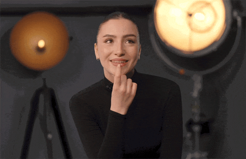 a woman in a black turtleneck is smiling with her finger on her lips