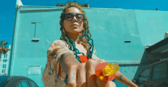 a woman with dreadlocks and sunglasses is holding a lollipop in front of a blue building
