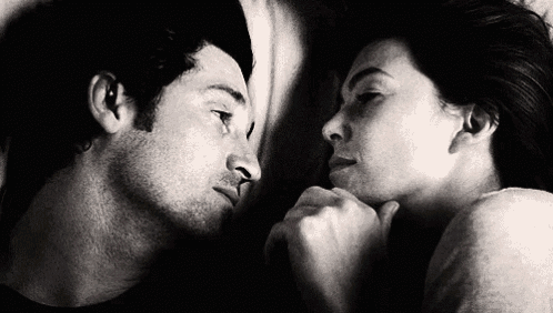 a man and a woman are laying next to each other and looking at each other in a black and white photo .