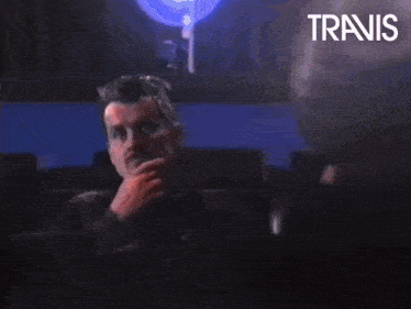 a man sits in a theater watching a movie and the word travis is on the bottom right